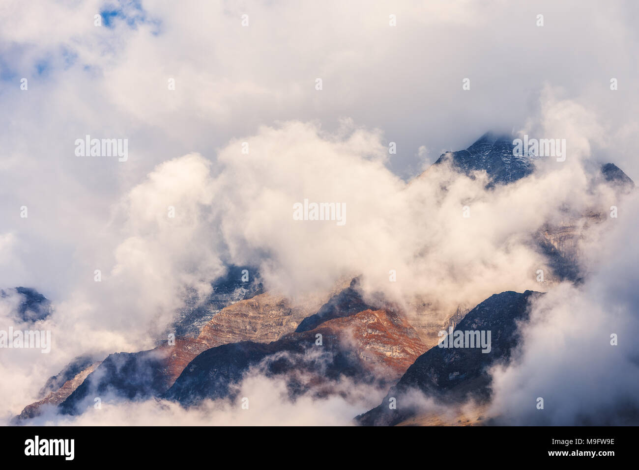 Mountains in clouds in overcast evening in Nepal. Landscape with beautiful high rocks and dramatic cloudy sky at sunset. Nature background. Fairy scen Stock Photo