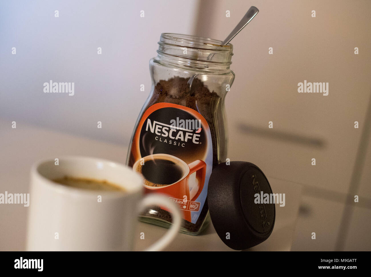25 March 2018, Germany, Munich A cup filled with instant coffee on a table with a jar of