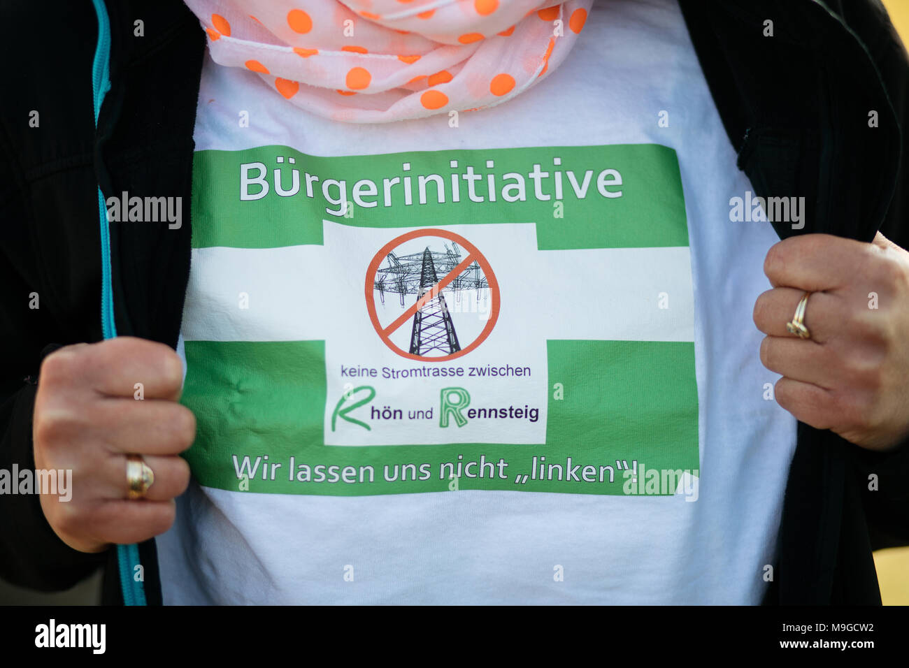 26 March 2018, Germany, Fambach: A member of the citizen initiative showing the logo on her t-shirt 'Keine Stromtrasse zwischen Rhön und Rennsteig' (lit. no power lines between Rhoen and Rennsteig). The demonstration is addressing the planned south link likes from network operator Tennet. Photo: Arifoto Ug/Michael Reichel/dpa Stock Photo