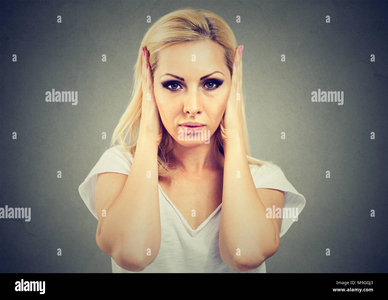 Young serious woman covering ears from rumors and noise avoiding problems and looking annoyed. Stock Photo