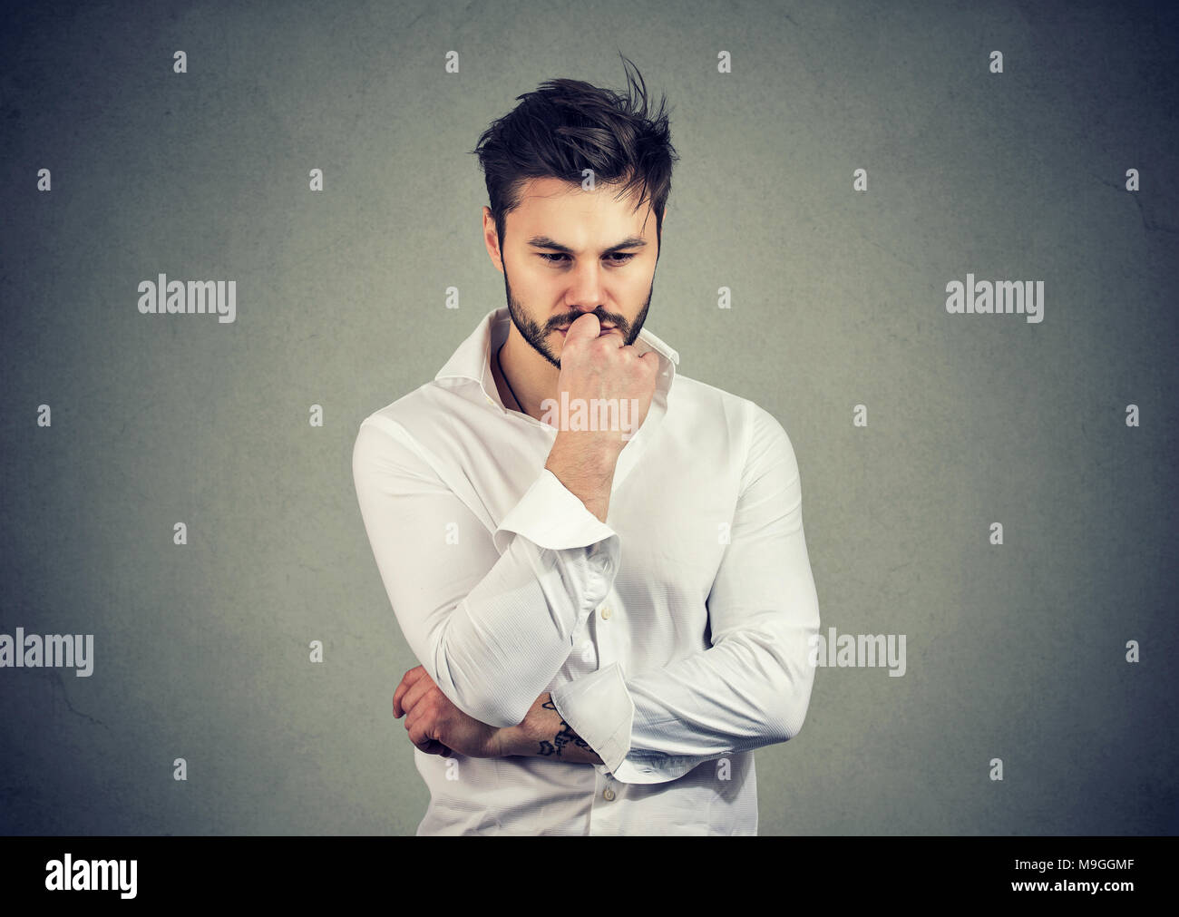 Young serious man touching lips and looking worried while solving big question in mind. Stock Photo