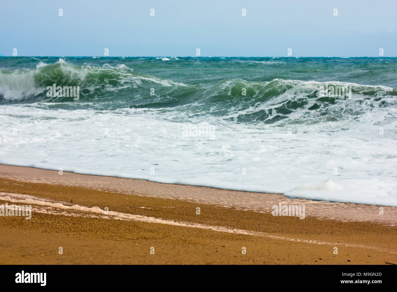 Stormy sea and blue sky, white sea foam on the yellow sandy beach. Stock Photo