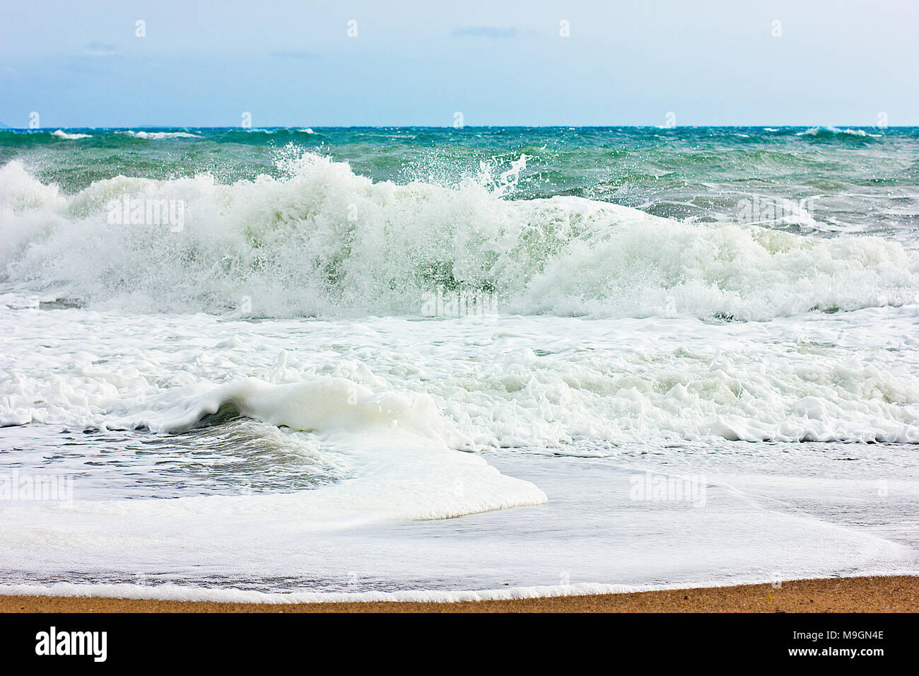 Stormy sea and blue sky, white sea foam on the yellow sandy beach. Stock Photo