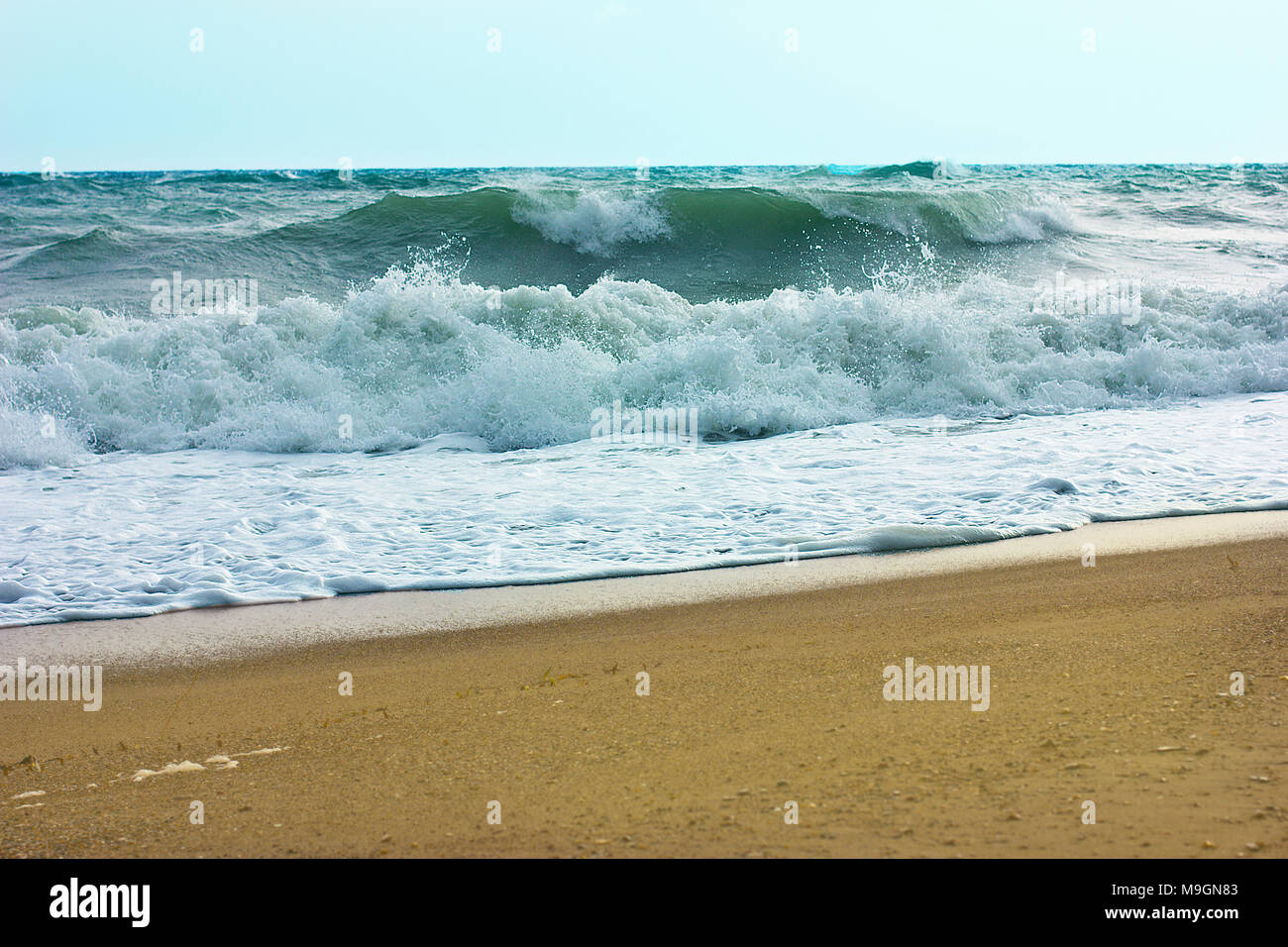 Stormy sea and blue sky, white sea foam on the yellow sandy beach. Stock Photo