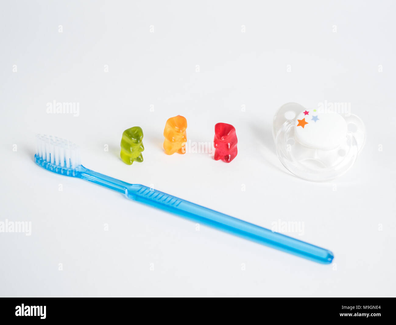 Three gummy bears, a pacifier and a blue toothbrush against a white background Stock Photo