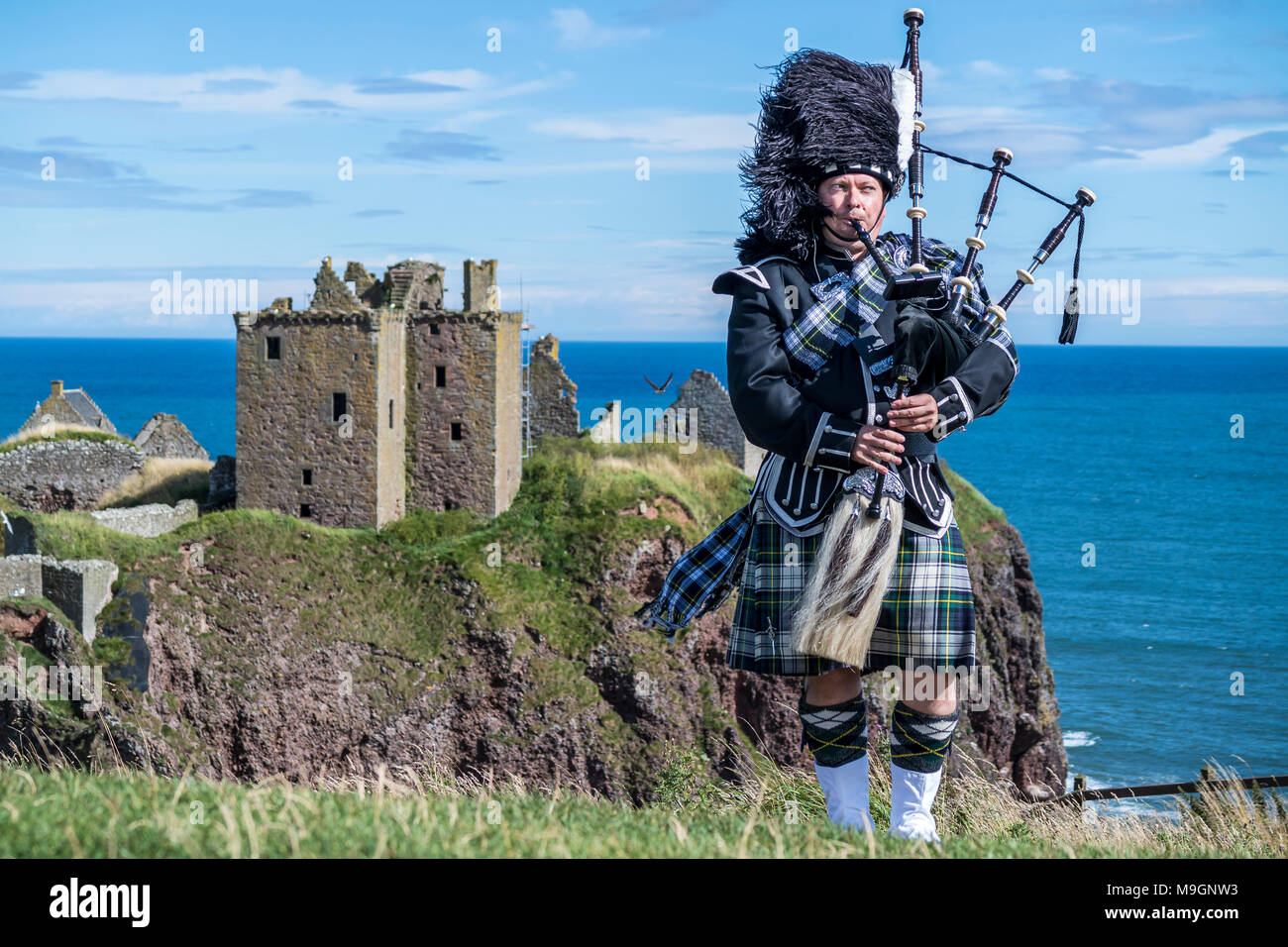 Traditional scottish bagpiper in full dress code at Dunnottar Castle in Stonehaven Stock Photo