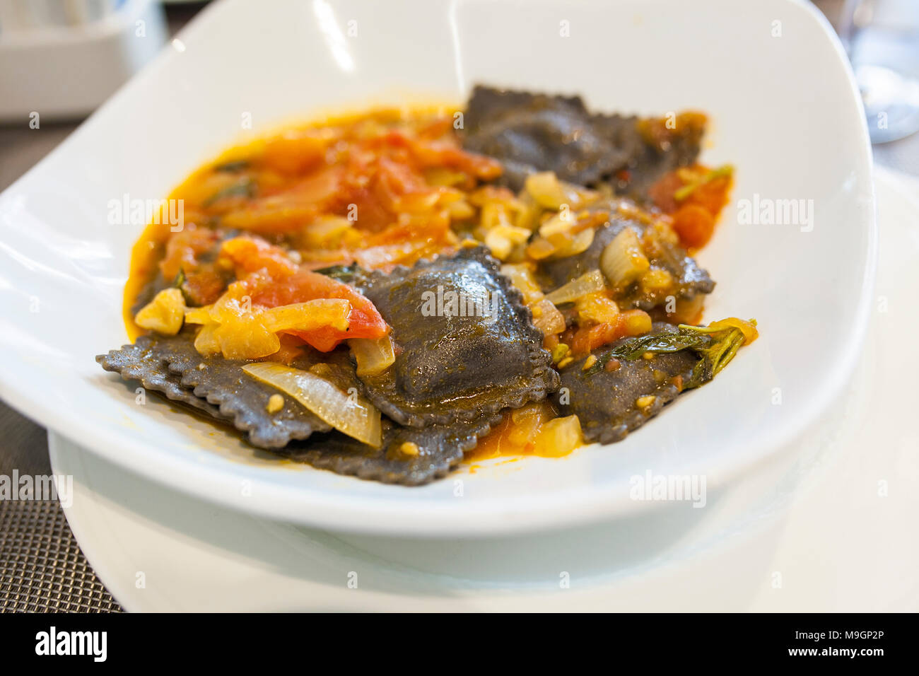 Dish of black squid ink ravioli with natural tomatoes sauce. Selective focus Stock Photo