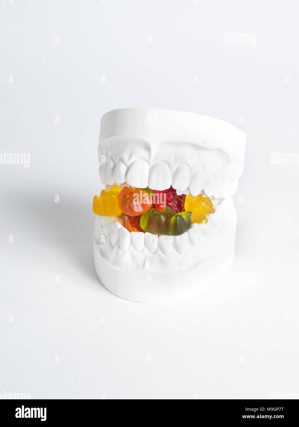 The plaster bit has gummy bears between its teeth against a white