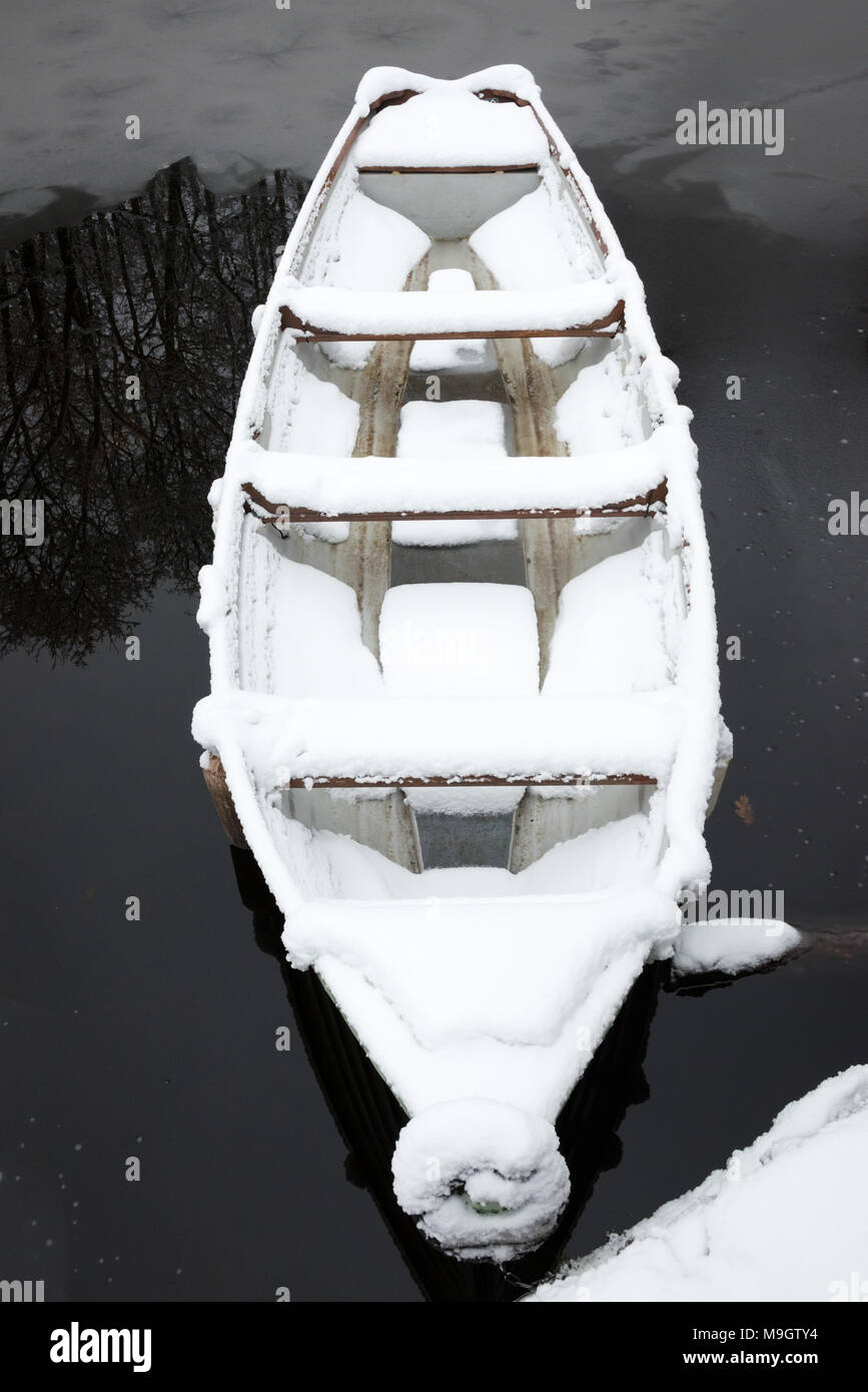 Lone moored boat covered in snow on water from above. Stock Photo