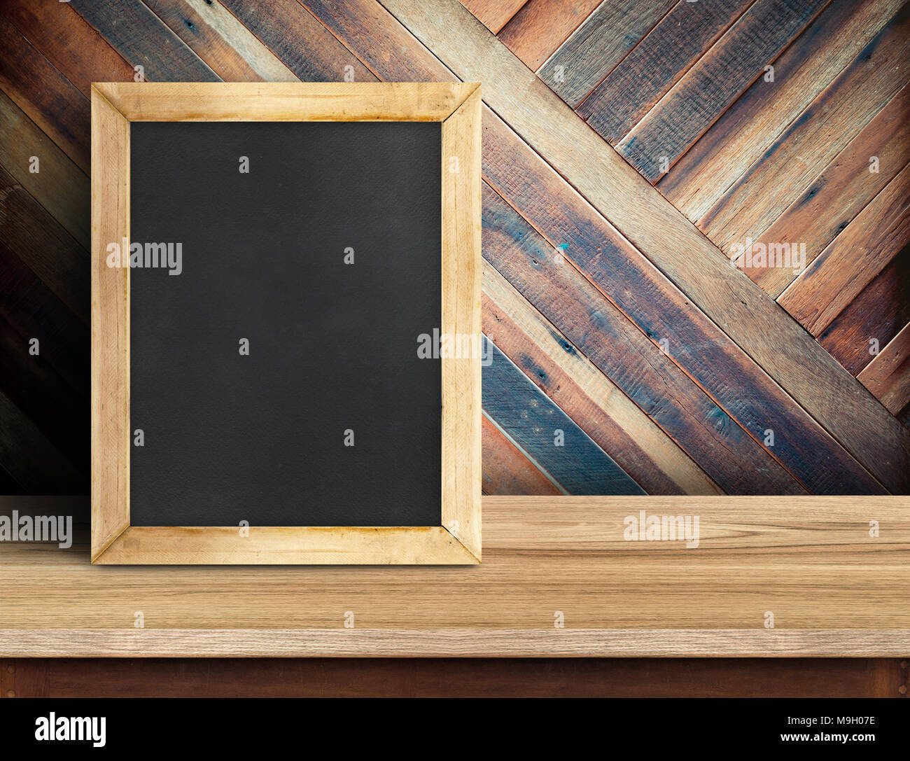 Blackboard on plank wooden table top at diagonal tropical wood wall,Template mock up for adding your design and leave space beside frame for adding mo Stock Photo