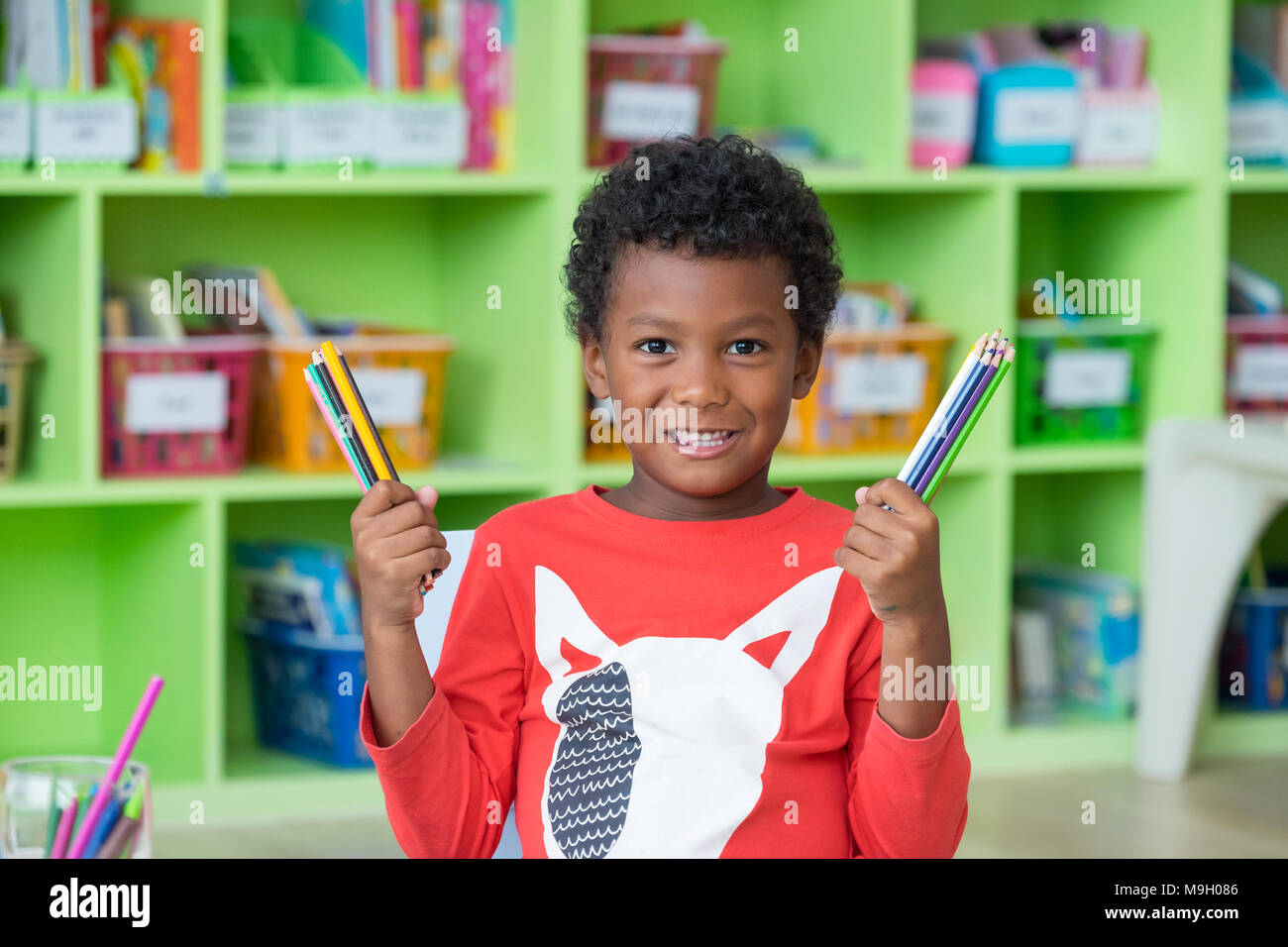 African American ethnicity kid holding group of color pencil smiling at library in kindergarten preschool classroom.education concept Stock Photo