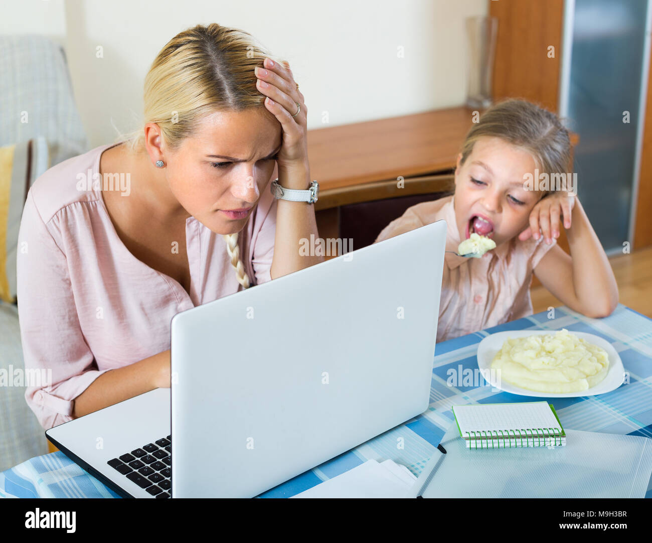 Tired businesswoman irritated as little daughter diverts her from work Stock Photo