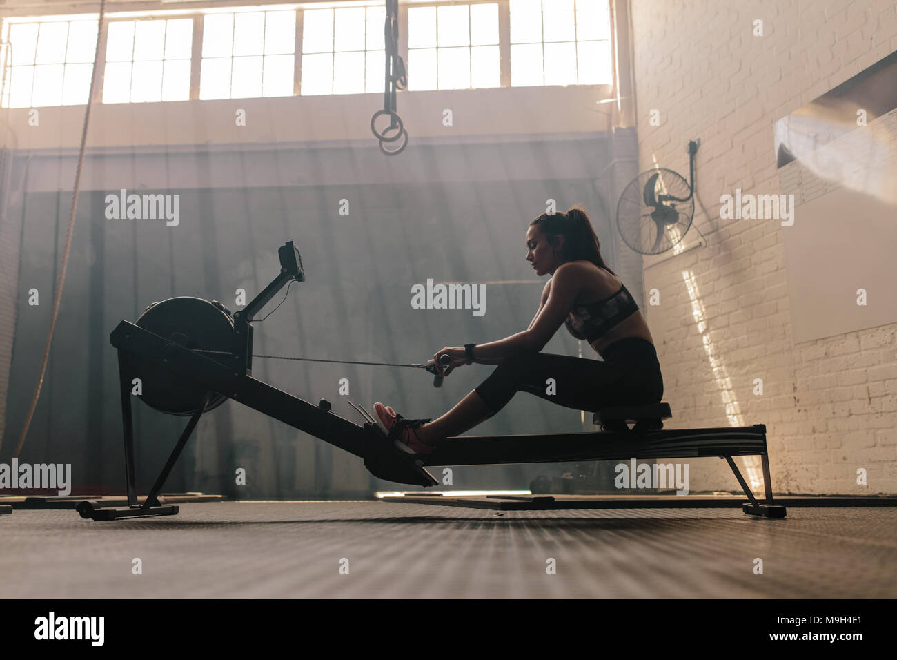 Fit young woman working out on a rowing machine at the gym. Female doing cardio exercise in fitness club. Stock Photo
