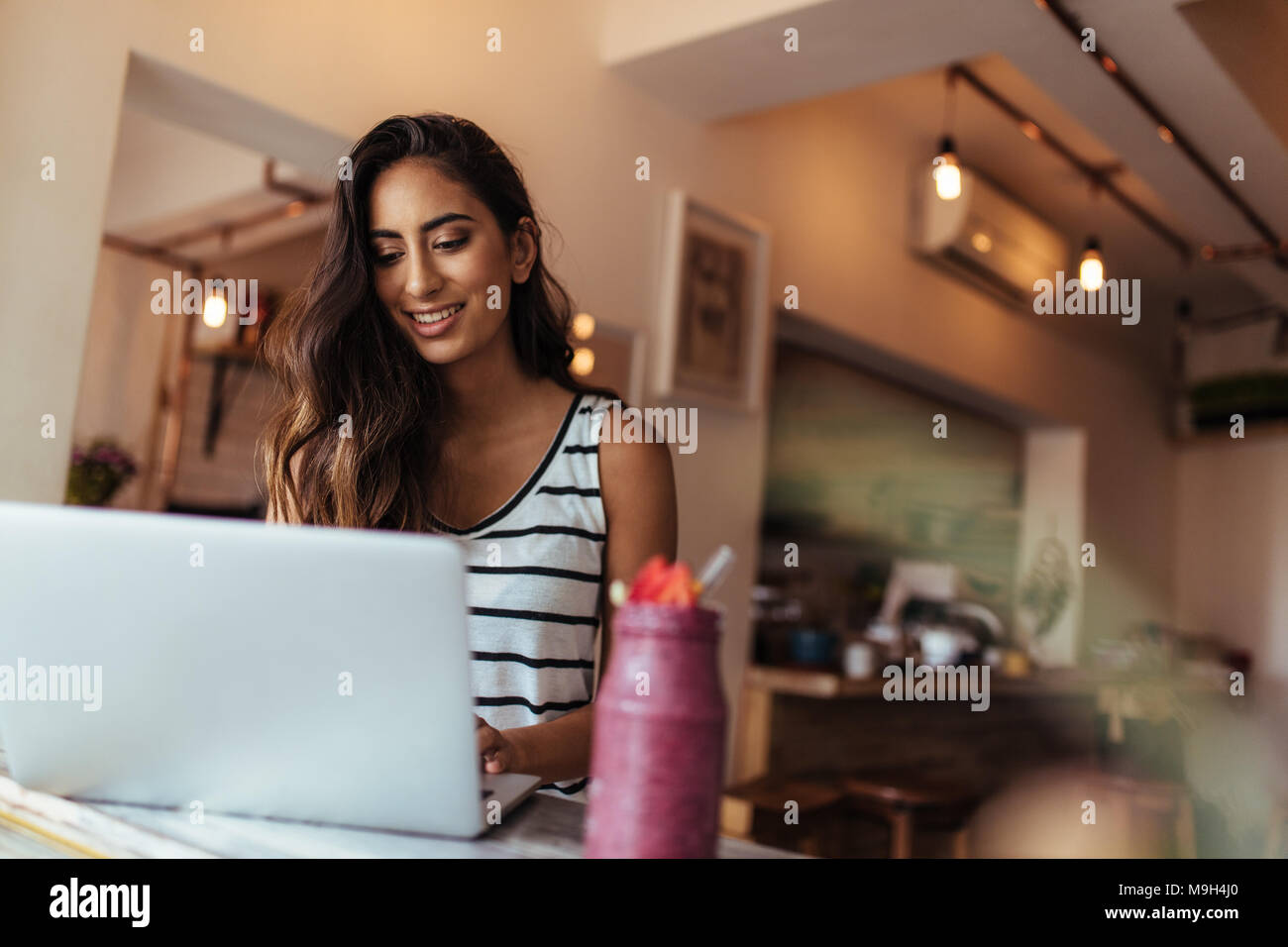 Woman entrepreneur working on laptop computer with a smoothie on the table. Woman enjoying a glass of smoothie while working. Stock Photo