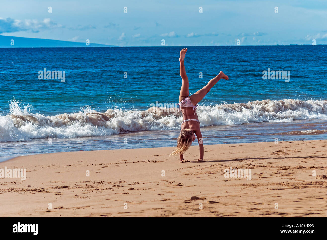 A tween girl does an almost perfect cartwheel on the beach, Maui Hawaii. USA Stock Photo