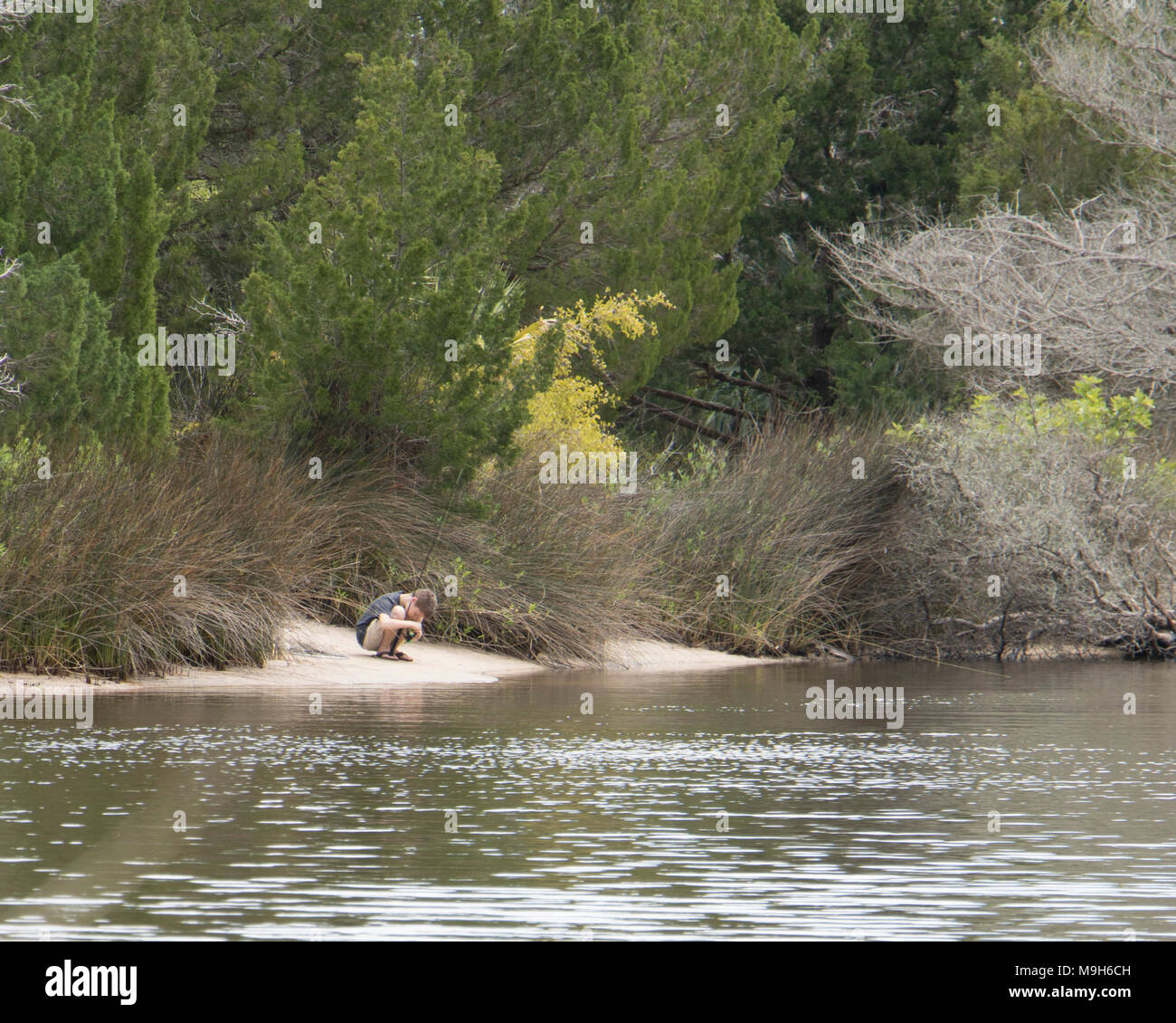 Gone Fishin’ Caucasian white male boy fishing in a lake surrounded by trees Stock Photo