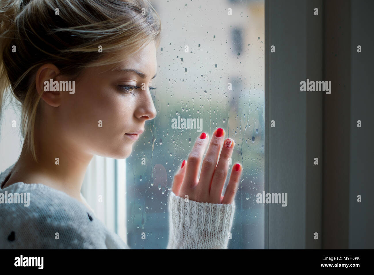Young girl looking out the window and feeling sad Stock Photo - Alamy
