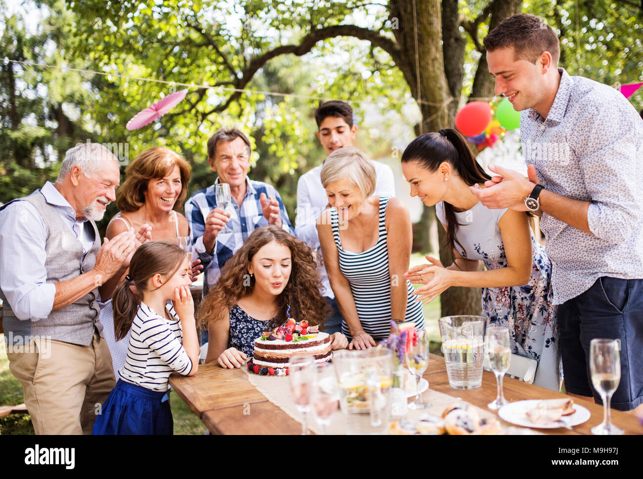 Family celebration outside in the backyard. Big garden party. Birthday party. A teenage girl with a birthday cake. Stock Photo