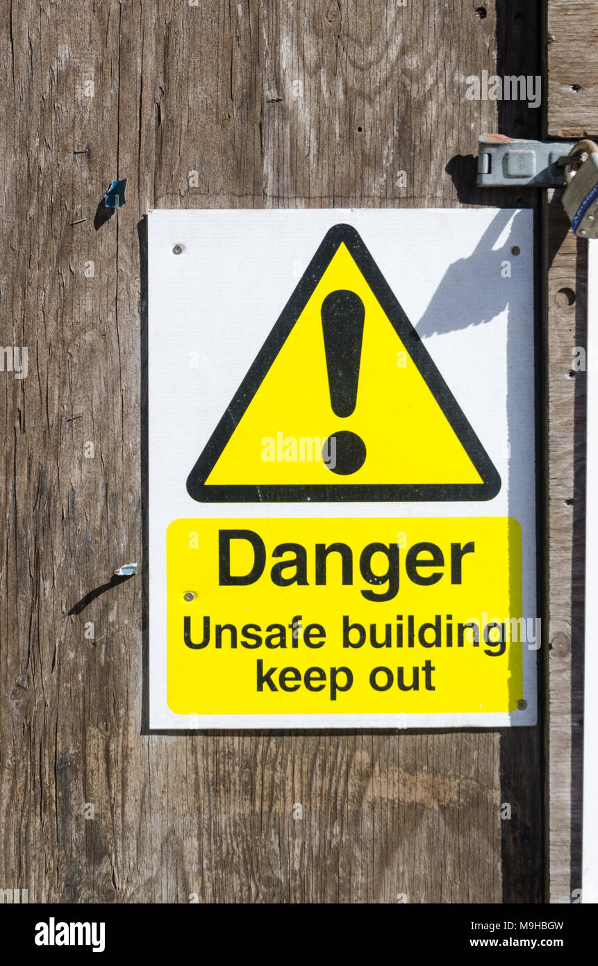 Warning sign saying Danger Unsafe building keep out attached to wooden door Stock Photo