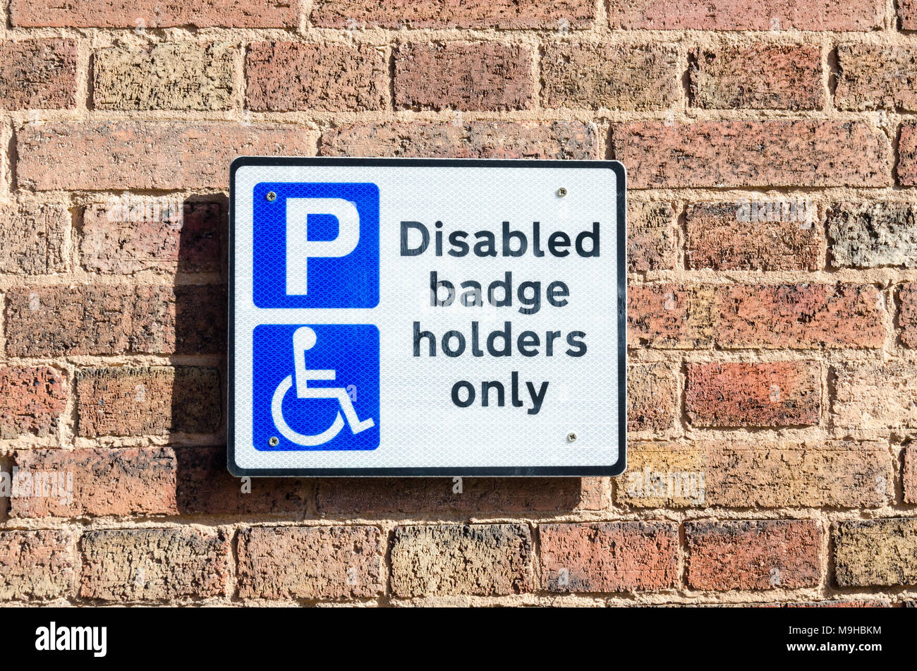 Sign on brick wall in car park saying parking for disabled badge ...