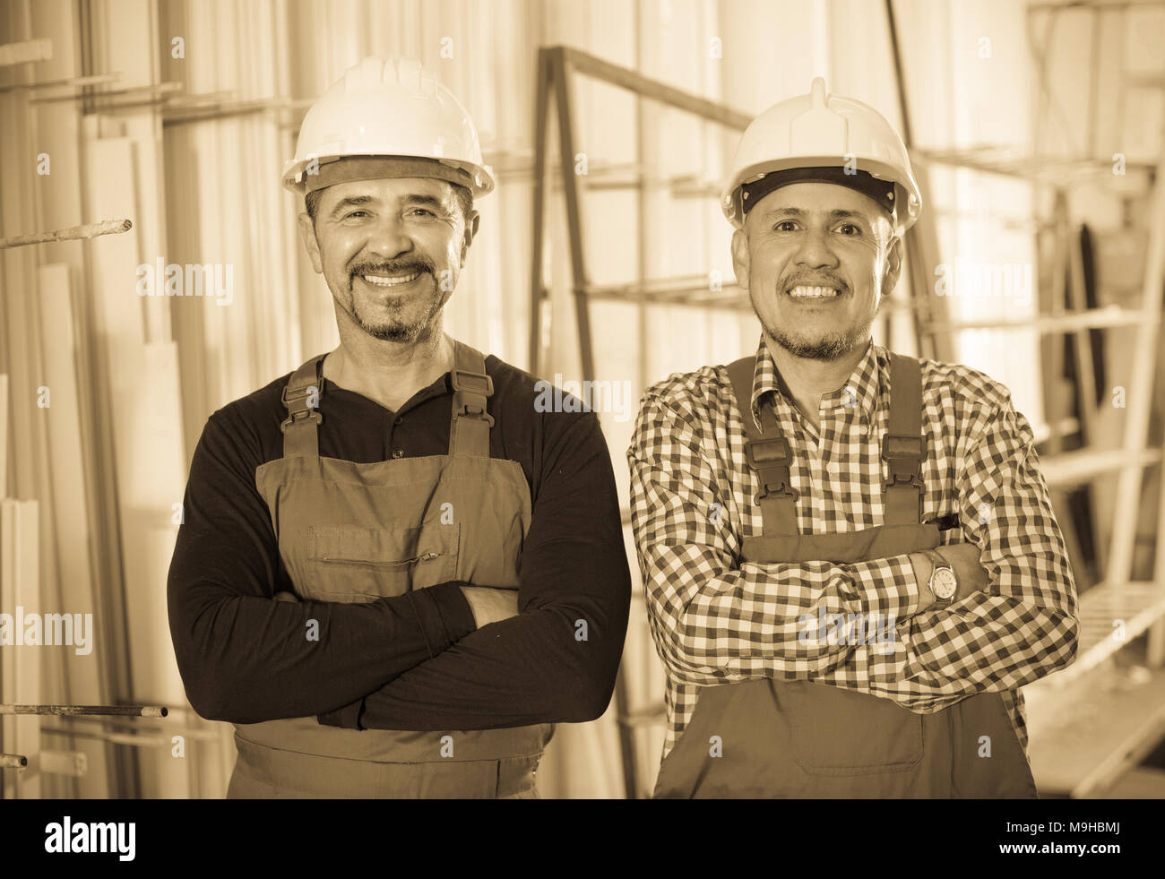 Two positive specialists in helmets and workwear posing at workshop Stock Photo