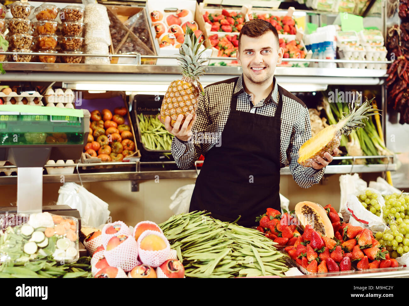 vigorous male seller showing assortment of fruits and vegetables in the ...