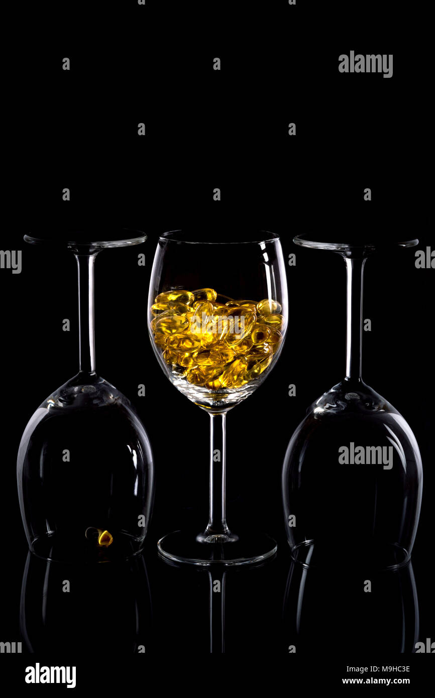 Three wine glasses with yellow pills against a black elegant background. Stock Photo