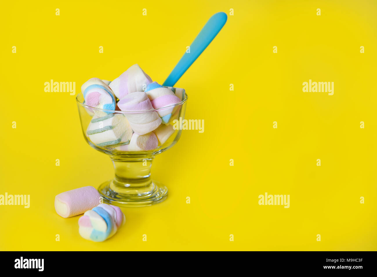 sweet marshmallows in a glass with a blue spoon, in a yellow background, with copy space Stock Photo