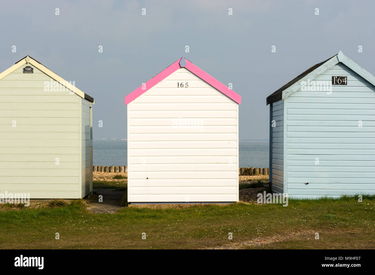 Three colourful beach huts in a row at Calshot Spit, Southampton, Hampshire, UK with a feminine looking on the the middle making a statement. Stock Photo