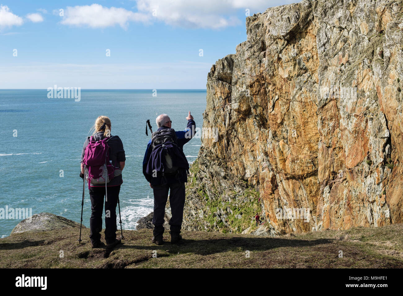 Two hikers looking at rock climbers on sea cliffs at Rhoscolyn Head. Rhoscolyn, Holy Island, Isle of Anglesey, north Wales, UK, Britain Stock Photo