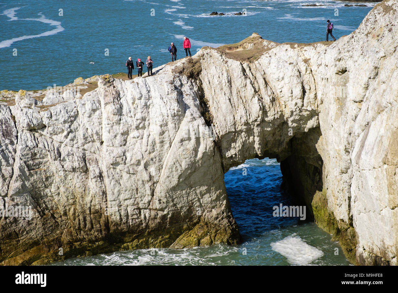 Group of Ramblers on Bwa Gwyn or White Arch natural rock formation on seacliffs along Isle of Anglesey Coastal Path. Rhoscolyn Anglesey north Wales UK Stock Photo