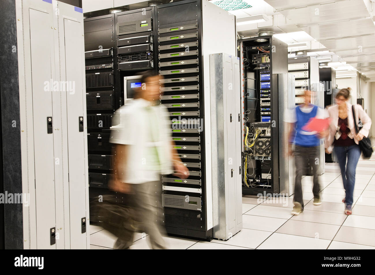 Three multi-ethnic technicians working in a large computer server room. Stock Photo