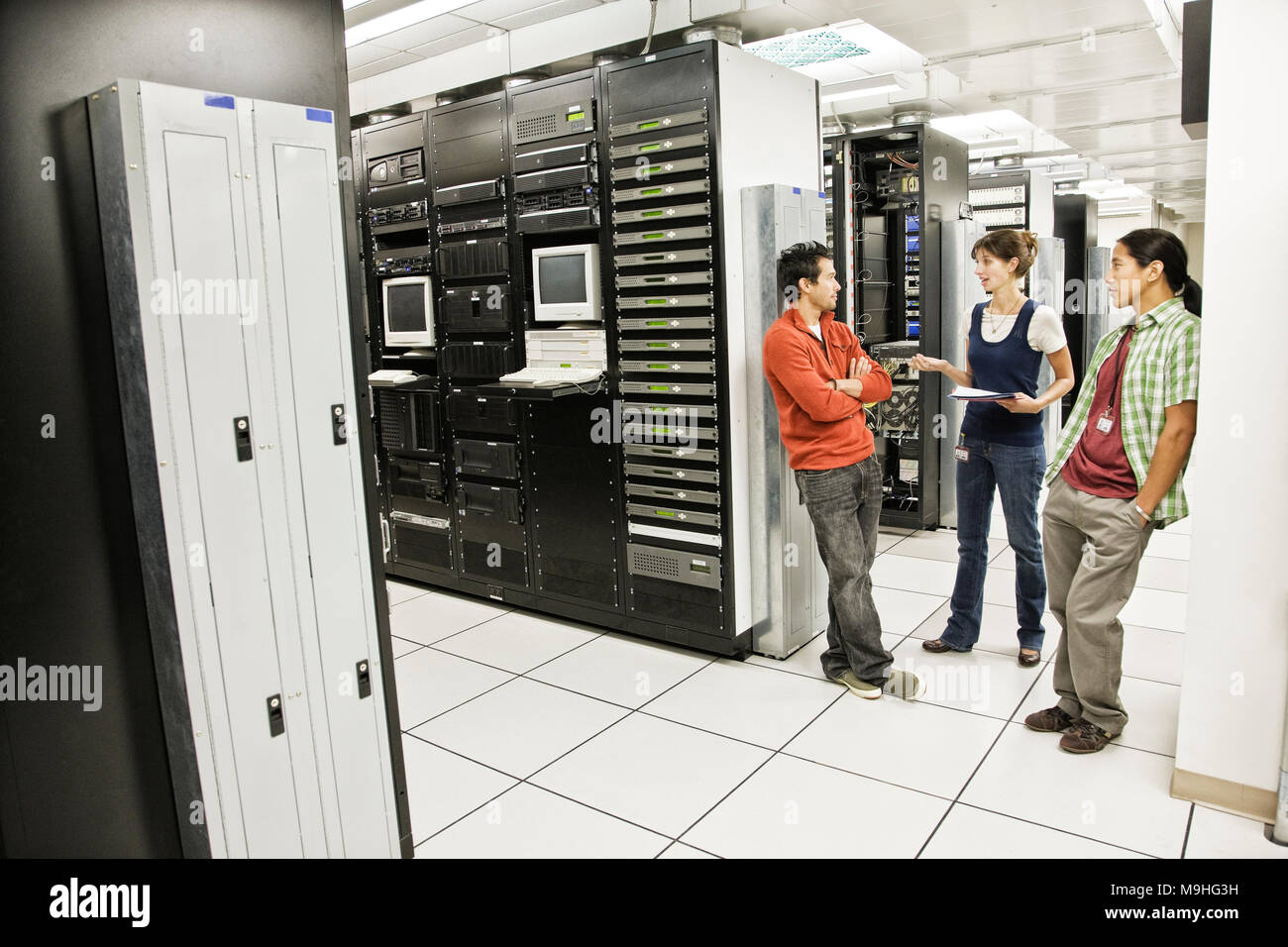 Three multi-ethnic technicians working in a large computer server room. Stock Photo