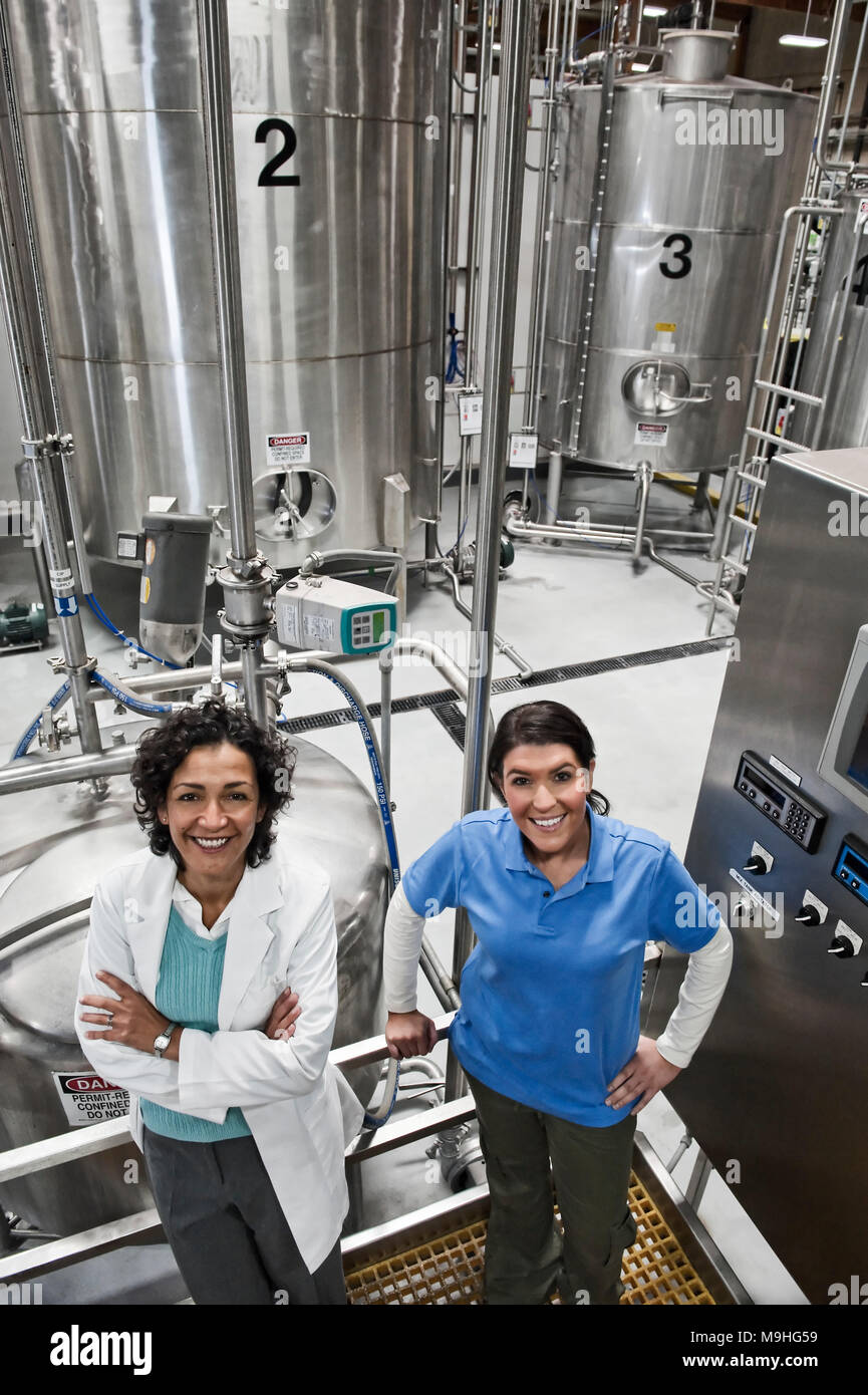 A portrait of a  multi-ethnic team of female technicians working near large processing tanks in a bottling plant. Stock Photo