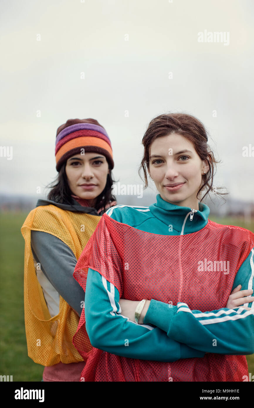 Portrait of two Caucasian women in sports clothing with team bibs of opposing teams and woolly hats side by side. Stock Photo