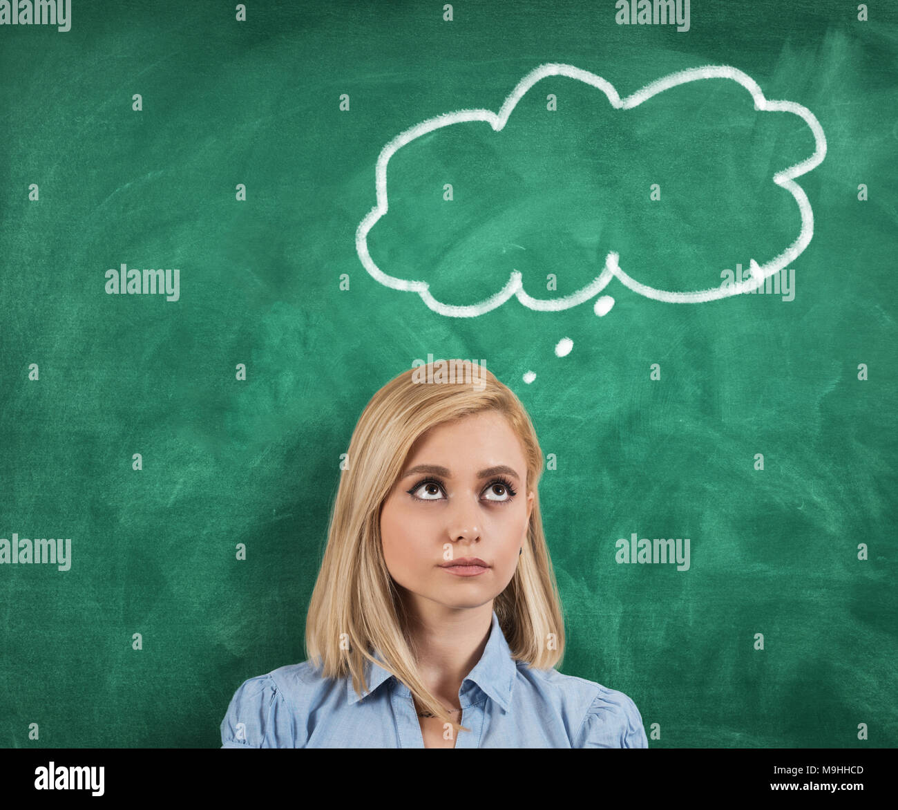 Young thoughtful woman standing on green blackboard. Stock Photo