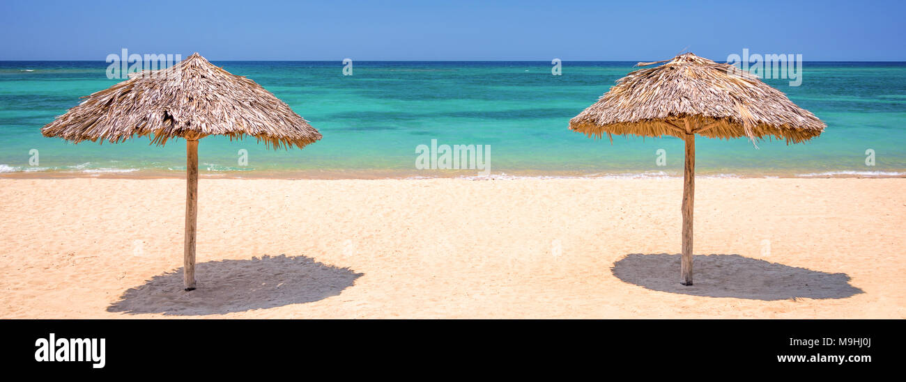 Two straw umbrellas on a beautiful tropical beach, panoramic travel