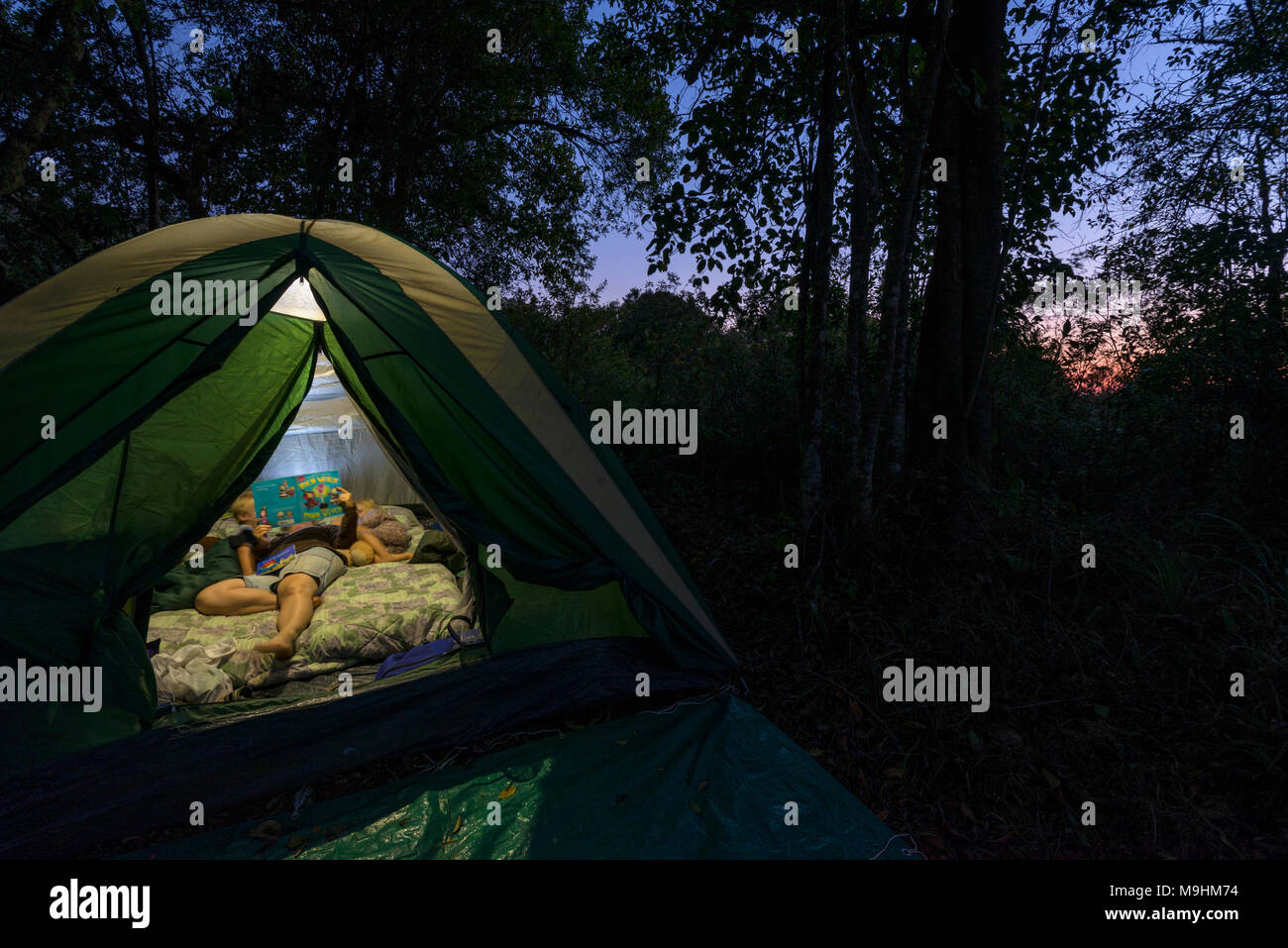 A mother reads a bedtime story to her children in a tent. Stock Photo