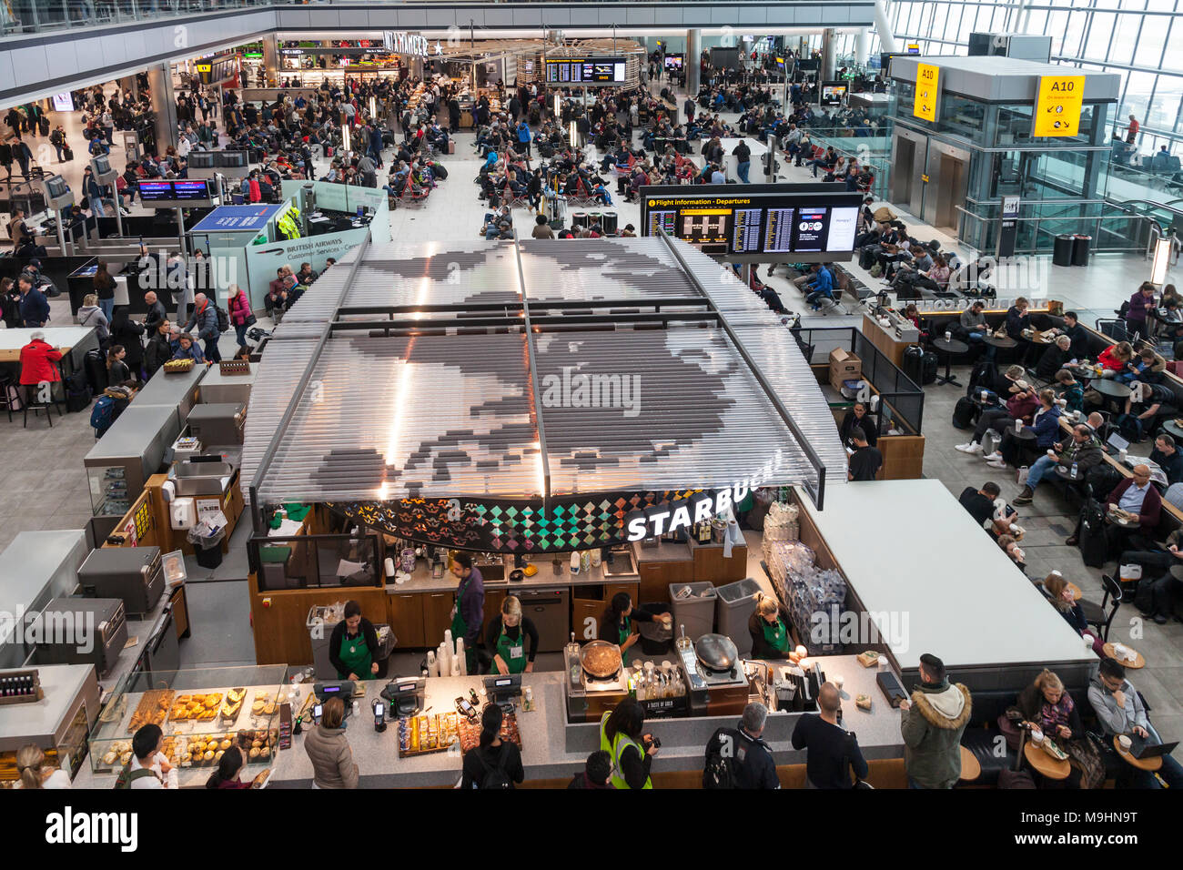 Heathrow Airport Terminal Five Departures Lounge and concourse. Large world map on roof of Starbucks outlet. Busy with passengers on a day of many fli Stock Photo