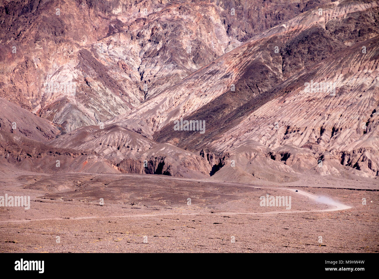 Two vehicles are driving towards the colourful eastern hills of Death Valley on a loose-surface road through a barren land Stock Photo