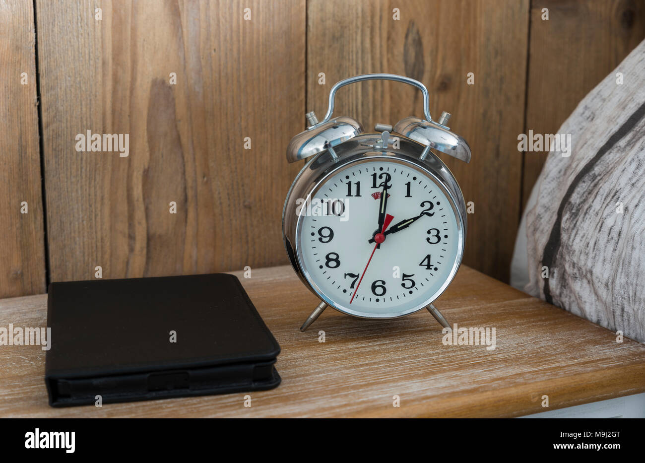 An old fashioned silver coloured bed side analogue pre digital alarm clock and modern ereader on bedside table Stock Photo