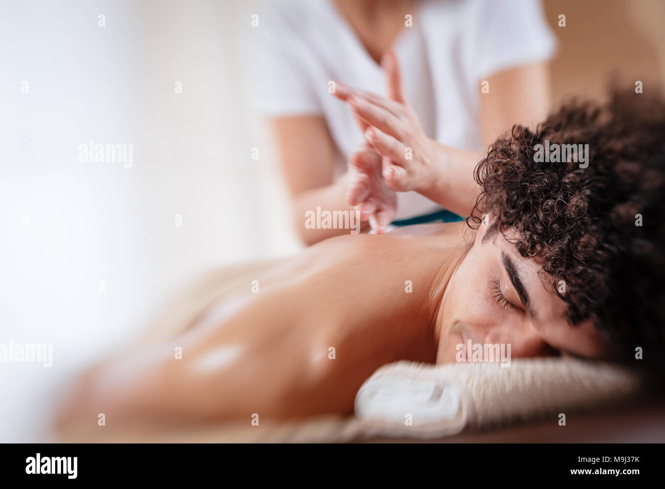 Close-up of a handsome healthy young man enjoying relaxing back massage at beauty salon. Selective focus. Stock Photo