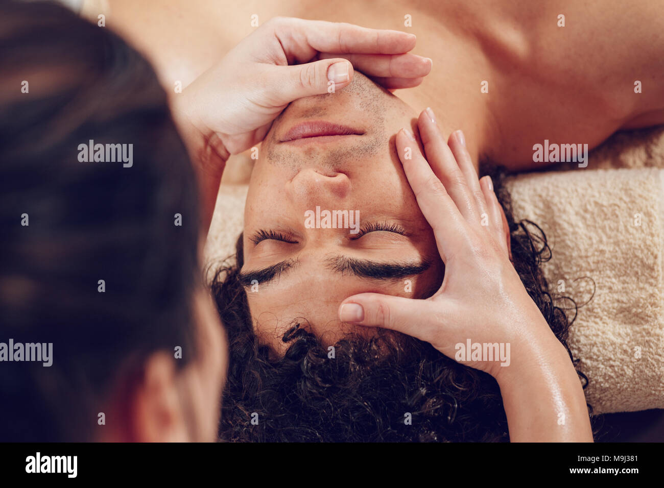 Close-up of a handsome healthy young man enjoying relaxing facial massage at beauty salon. Top view. Stock Photo