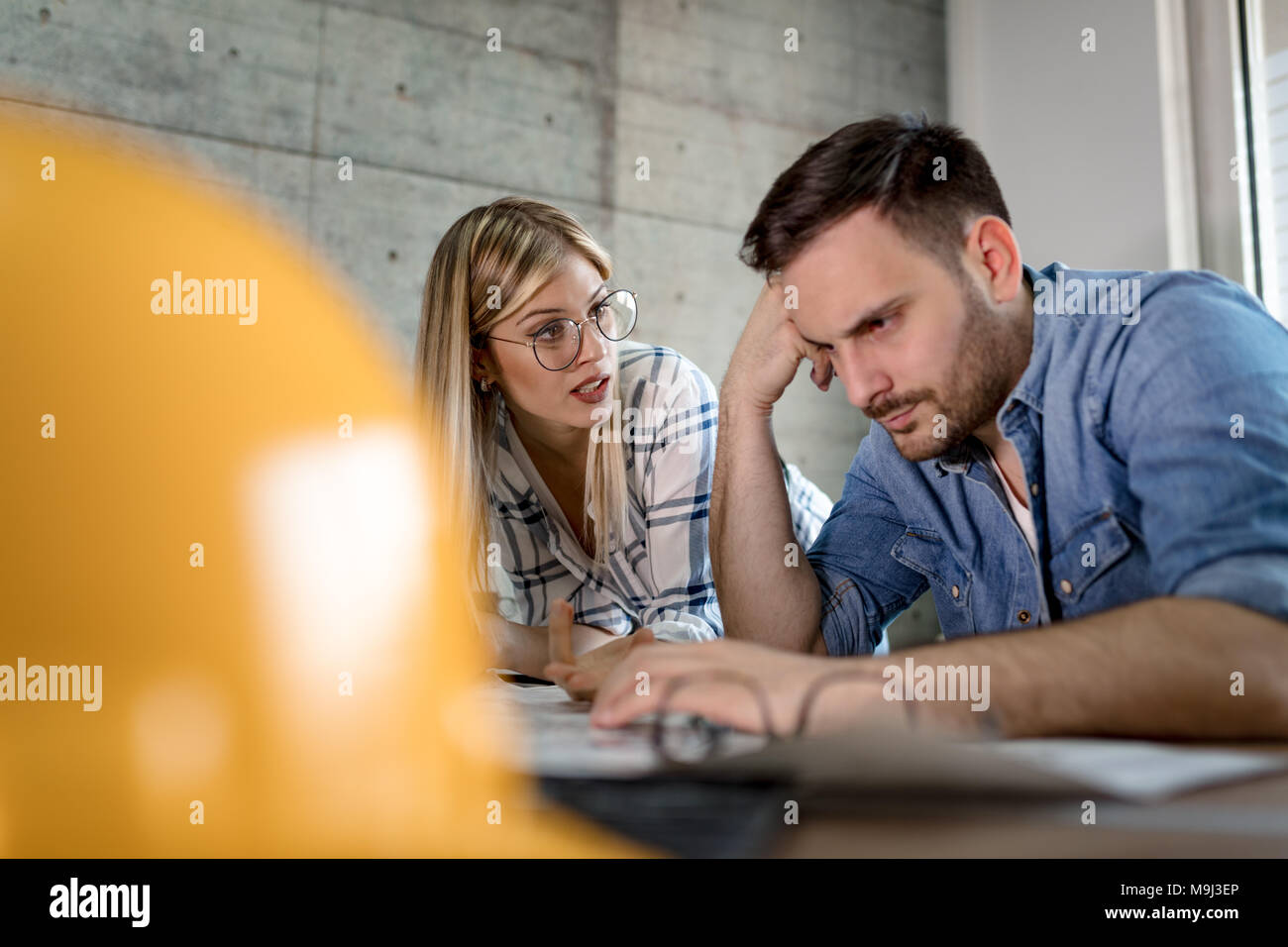 Young worried architect colleagues talking and analyzing blueprints while working on a new project at the office. Stock Photo