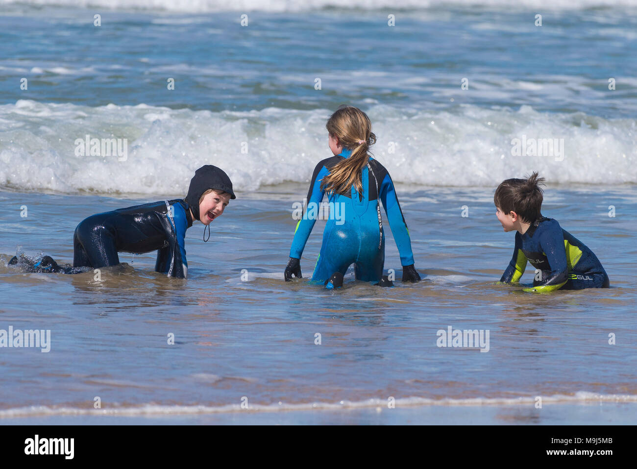 Children wearing wetsuits playing in the sea at Fistral Beach in Newquay Cornwall. Stock Photo