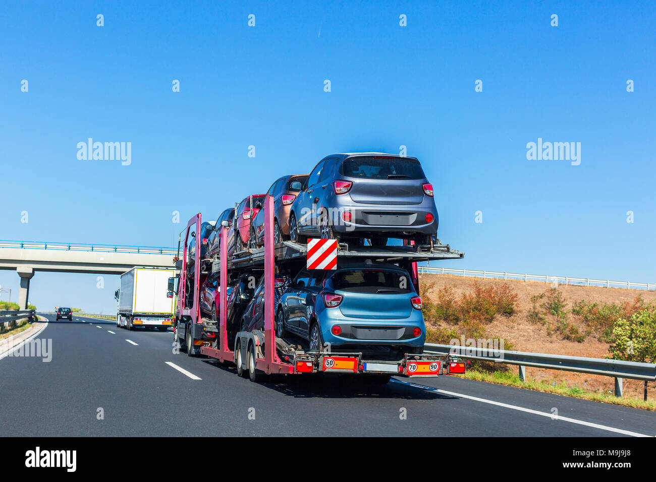 Car carrier trailer with cars on bunk platform. Car transport truck on the highway. Highway bridge. Space for text Stock Photo