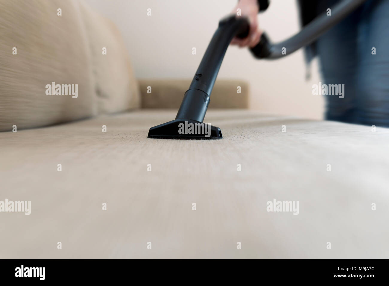 Woman cleaning the sofa, couch with vacuum cleaner Stock Photo