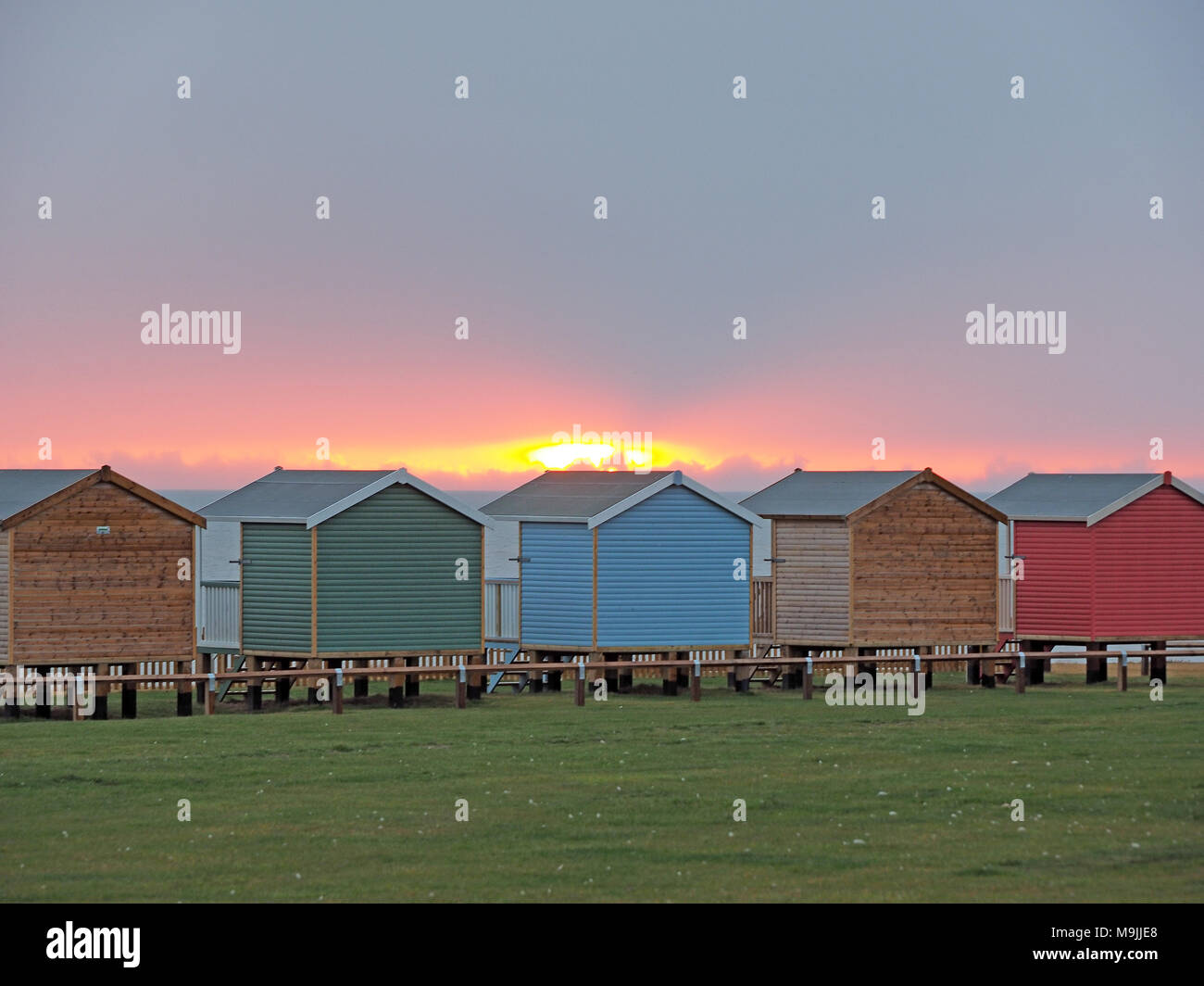 Leysdown, Kent, UK. 27th March, 2018. UK Weather: on a cold and wet morning, the clouds parted briefly to allow the sun to shine through creating a stunning sunrise over the beach huts of Leysdown, before disappearing again only moments later. Credit: James Bell/Alamy Live News Stock Photo