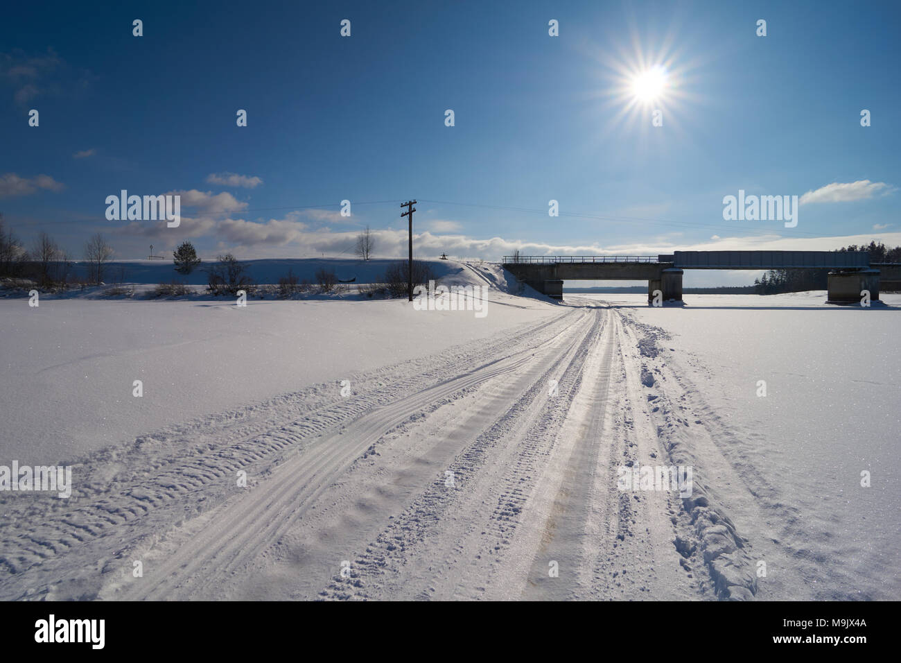 Ice road and railway bridge on Zhukopa river in winter with direct sun in the photograph, Peno district, Tver oblast, Russia Stock Photo