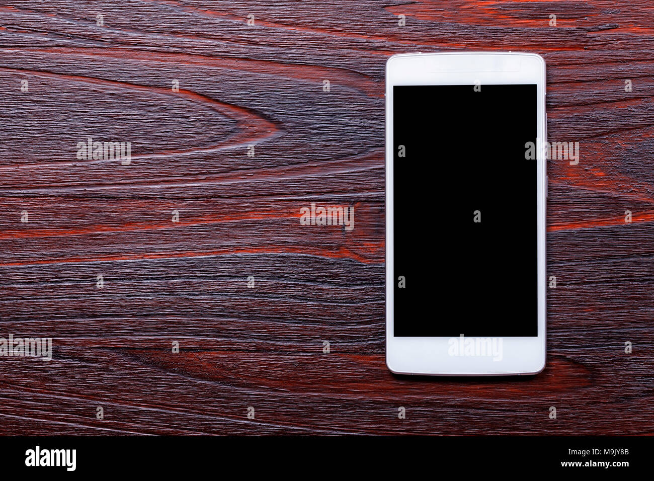 White smart phone template with black screen on top of a mahogany wood table. Stock Photo